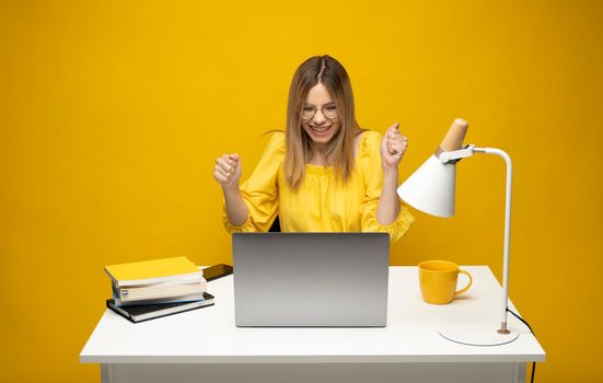 Young successful happy employee business woman in casual yellow shirt sit work at office desk with pc laptop computer workspace area do winner gesture