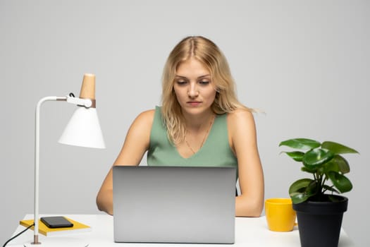 Smiling business woman working with a laptop isolated on a grey background. Portrait of a pretty young woman studying while sitting at the table with grey laptop computer, notebook.