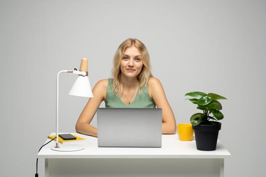 Portrait of a pretty young woman studying while sitting at the table with grey laptop computer, notebook. Smiling business woman working with a laptop isolated on a grey background