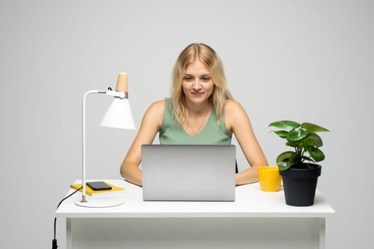 Portrait of a pretty young woman studying while sitting at the table with grey laptop computer, notebook. Smiling business woman working with a laptop isolated on a grey background