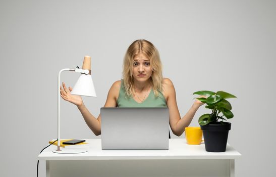 Confused young attractive business woman or student with a blond hair sitting at the table and working on a laptop. Young cheerful student girl . Studying