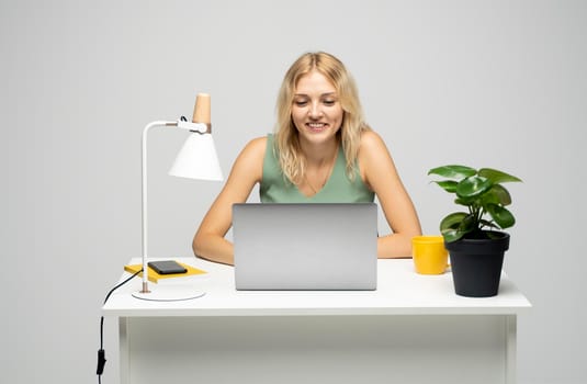 Portrait of a pretty young woman studying while sitting at the table with grey laptop computer, notebook. Smiling business woman working with a laptop isolated on a grey background