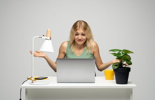 Confused blonde business woman working on a laptop on a white background