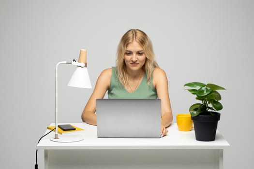 Portrait of a pretty young woman studying while sitting at the table with grey laptop computer, notebook. Smiling business woman working with a laptop isolated on a grey background