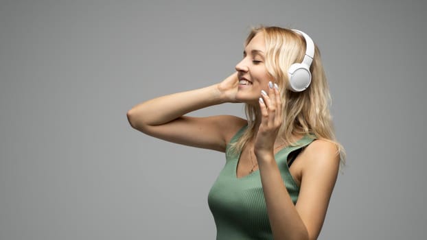 Beautiful young woman listening to music in headphones on grey background