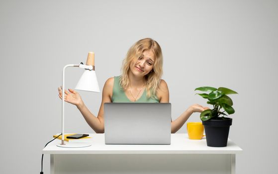 Confused young attractive business woman or student with a blond hair sitting at the table and working on a laptop. Young cheerful student girl . Studying