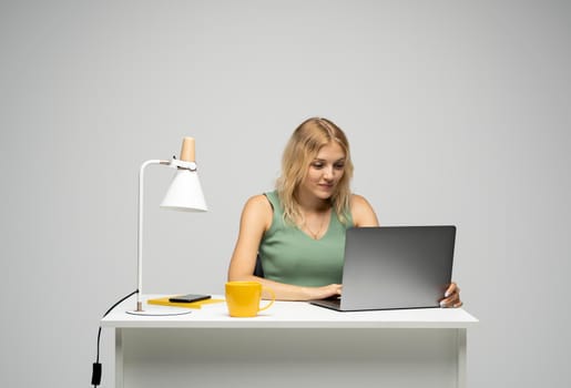 Portrait of a pretty young woman studying while sitting at the table with grey laptop computer, notebook. Smiling business woman working with a laptop isolated on a grey background