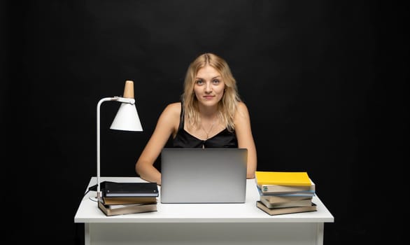 Smiling business woman working with a laptop isolated on a grey background. Portrait of a pretty young woman studying while sitting at the table with grey laptop computer, notebook.