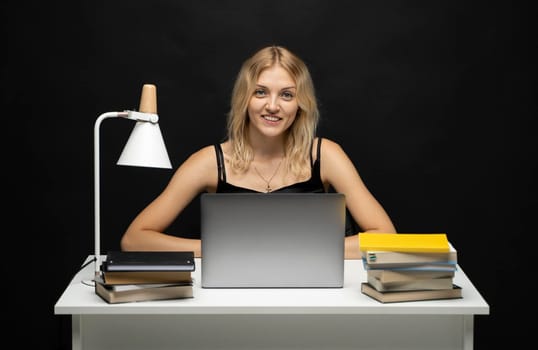 Portrait of Smiling pretty young woman studying while sitting at the table with grey laptop computer, notebook. Business woman working with a laptop isolated on a yellow background