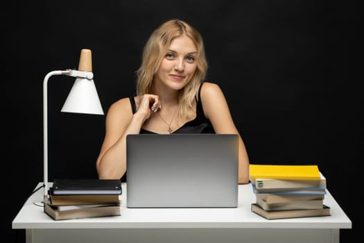 Portrait of Smiling pretty young woman studying while sitting at the table with grey laptop computer, notebook. Business woman working with a laptop isolated on a yellow background