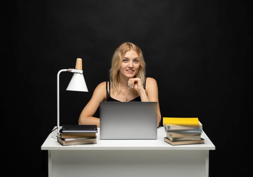 Portrait of Smiling pretty young woman studying while sitting at the table with grey laptop computer, notebook. Business woman working with a laptop isolated on a yellow background