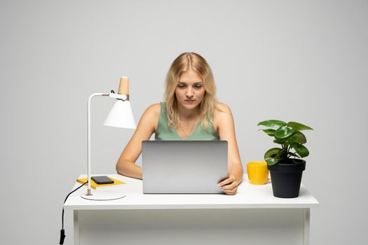 Portrait of a pretty young woman studying while sitting at the table with grey laptop computer, notebook. Smiling business woman working with a laptop isolated on a grey background