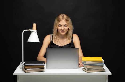 Smiling business woman working with a laptop isolated on a grey background. Portrait of a pretty young woman studying while sitting at the table with grey laptop computer, notebook.