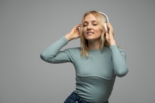 Beautiful dancing young woman listening the music in wireless headphone on dark grey background