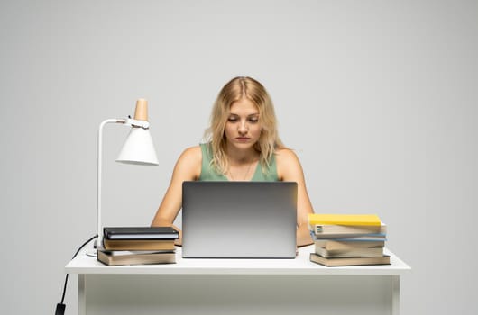 Portrait of a pretty young woman studying while sitting at the table with grey laptop computer, notebook. Smiling business woman working with a laptop isolated on a grey background