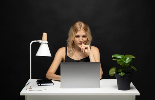 Portrait of a pretty young woman studying while sitting at the table with grey laptop computer, notebook. Smiling business woman working with a laptop isolated on a grey background