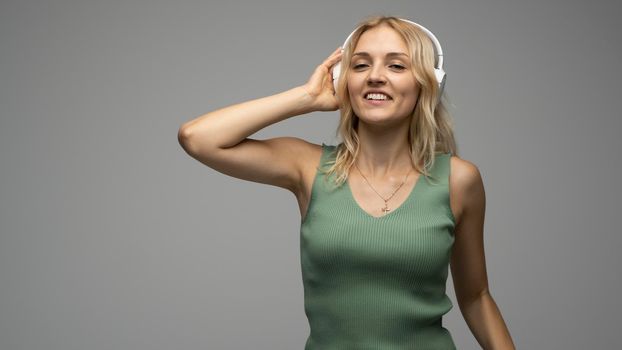 Beautiful blonde girl in green t-shirt in headphones having fun in studio dancing and laughing