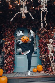 Girl with a pumpkin head posing at the door on the street . Halloween Concept