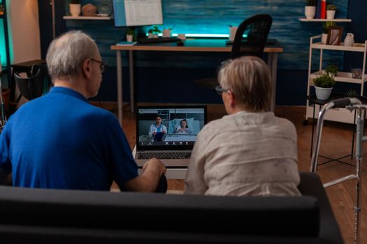 Retired couple chatting with doctor and niece on video call conference using laptop at home. Elder man and woman discussing child healthcare with medic from hospital on online communication