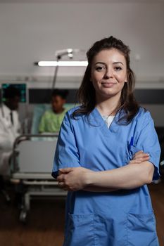 Portrait of specialist therapist nurse standing in hospital ward during medical appointment. In background doctor consulting sick patient discussing healthcare treatment. Medicine services