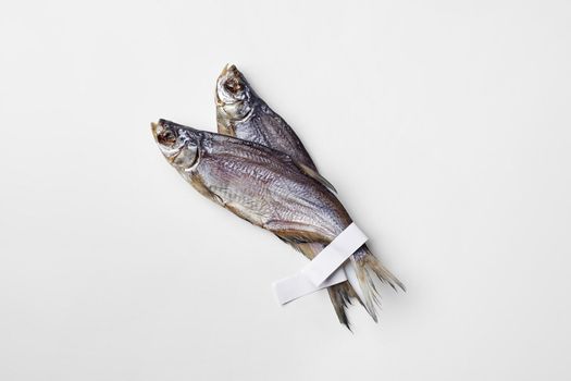 Two salted jerked roach fish with paper labels on tails isolated on white background with copyspace. Popular fish snack concept