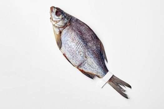 One whole salted sun-dried bream with label on tail lying on white surface, top view with copyspace