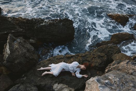 Barefoot woman in a secluded spot on a wild rocky coast in a white dress unaltered. High quality photo