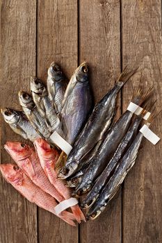 Heap of jerked and dried salted roach, sabrefish and red mullets with labels on tails lying on rough wooden boards background