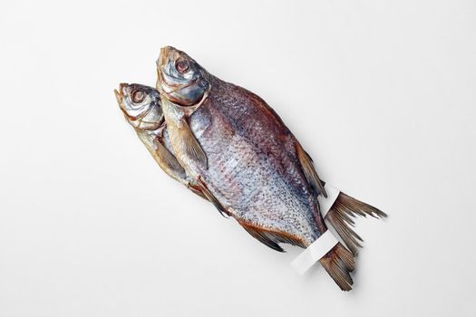 Two whole salted sun-dried breams with paper labels on tails lying on white background, top view with copyspace