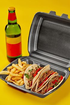 Birria tacos from tortillas filled with tender veal stew, fresh vegetables and greens served in takeaway container with fries and bottle of drink isolated on yellow background. Food delivery concept