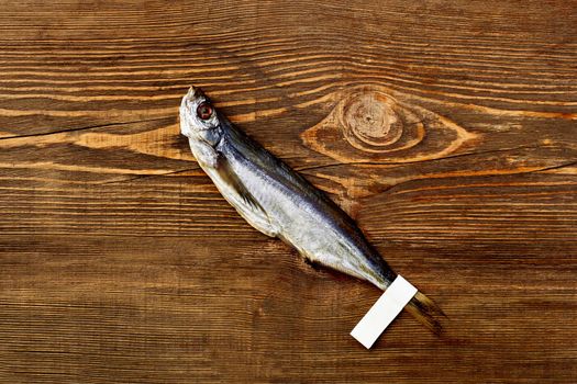 One salted dried sabrefish with paper label on tail lying on brown wooden surface, top view with copyspace