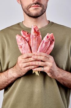 Young bearded man holding bunch of air-dried salted red mullets in hands. Concept of popular fish snacks