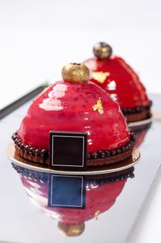 Delicious dessert on chocolate and nut shortcrust base with airy plum mousse covered with pink fruit glaze decorated with edible gold. Sweet pastry concept