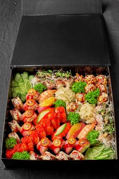Set of various Japanese sushi rolls with pickled ginger, fresh cucumber, lime slice and greens in cardboard box. Concept of food delivery