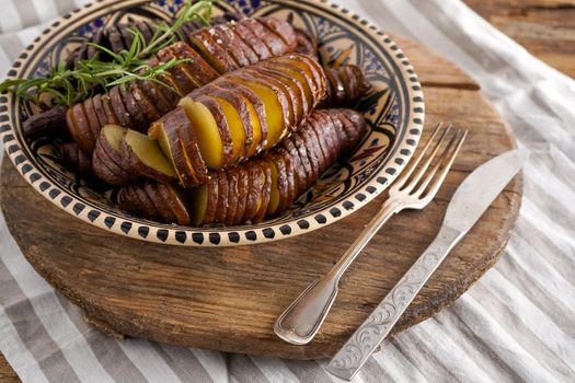 Sweet potato - sweet potatos tubers cooked in a pan. Fried and baked with spices and salt. Cut into pieces and slices. Healthy food close-up top view. Potato meal in a plate on a wooden table. Fork and knife.