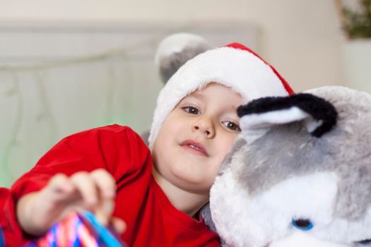 Portrait of a cute boy in a Santa Claus hat. Funny smiling child. Gifts, toys, joy, celebration. Christmas concert.