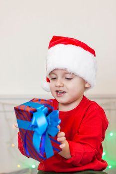 Portrait of a cute boy in a Santa Claus hat. Funny smiling child. Gifts, toys, joy, celebration. Christmas concert.