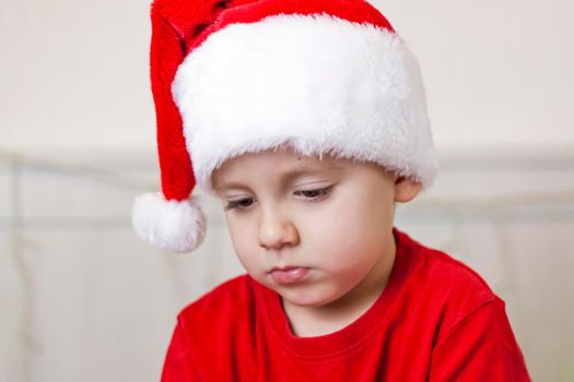 Portrait of a cute boy in a Santa Claus hat. Funny smiling child. Gifts, toys, joy, celebration. Christmas concert.