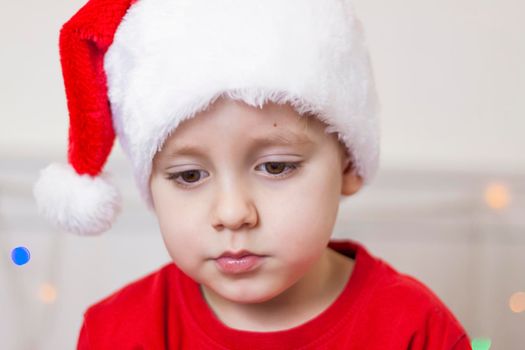 Portrait of a cute boy in a Santa Claus hat. Funny smiling child. Gifts, toys, joy, celebration. Christmas concert.