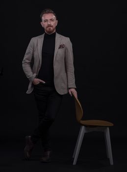 Portrait of adult businessman wearing trendy suit and sitting in modern studio on stylish chair against the black background. Horizontal mockup. High quality photo