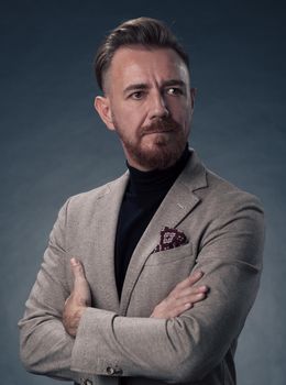 Portrait of a successful stylish elegant senior businessman with a grey beard and casual business clothes confident in photo studio isolated on dark background gesturing with hands. High-quality photo