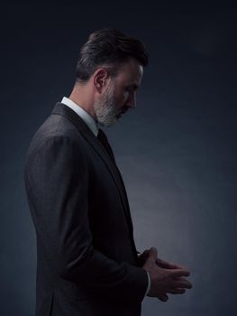 Portrait of a successful stylish elegant senior businessman with a grey beard and casual business clothes confident in photo studio isolated on dark background gesturing with hands. High-quality photo