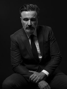 Portrait of a successful stylish elegant senior businessman with a grey beard and casual business clothes confident in photo studio isolated on dark background gesturing with hands. High-quality photo