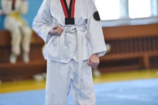 Taekwondo kids. A boy athlete stands in a taekwondo uniform with a white belt during a taekwondo tournament.