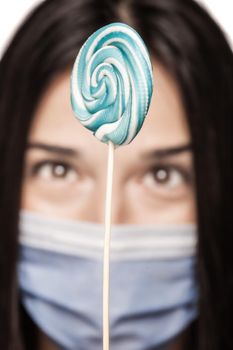 Girl having her mouth covered with with medical face mask holding lollipop
