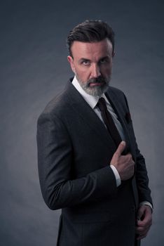 Portrait of a successful stylish elegant senior businessman with a grey beard and casual business clothes confident in photo studio isolated on dark background gesturing with hands. High-quality photo