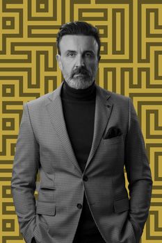 Black and white portrait of a stylish elegant senior businessman with a beard and casual business clothes against retro colorful pattern design background gesturing with hands. High quality photo