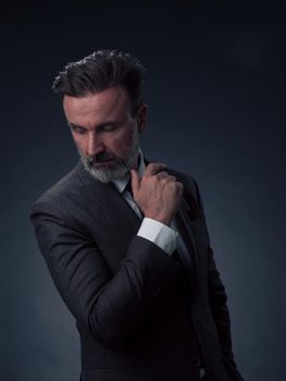 Portrait of a successful stylish elegant senior businessman with a grey beard and casual business clothes confident in photo studio isolated on dark background gesturing with hands. High-quality photo