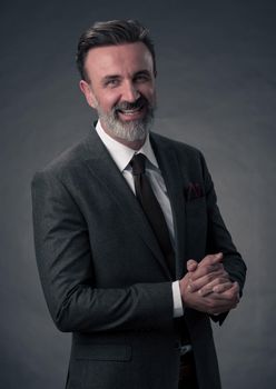 Portrait of a successful stylish elegant senior businessman with a grey beard and casual business clothes confident in photo studio isolated on dark background gesturing with hands. High-quality photo