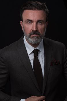 Portrait of a successful stylish elegant senior businessman with a grey beard and casual business clothes confident in photo studio isolated on dark background gesturing with hands. High-quality photo